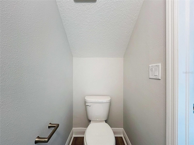 bathroom featuring a textured wall, baseboards, toilet, and a textured ceiling