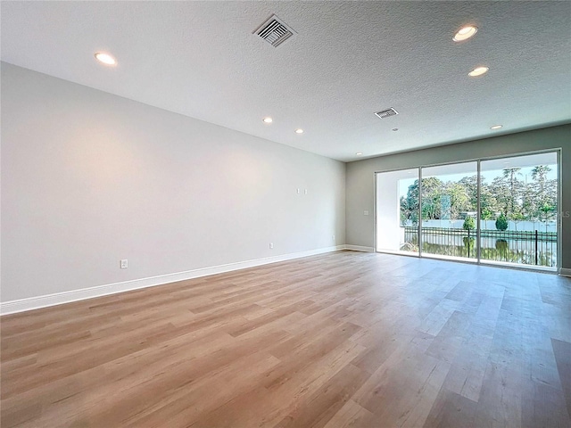 unfurnished room featuring light wood-type flooring, visible vents, a textured ceiling, recessed lighting, and baseboards