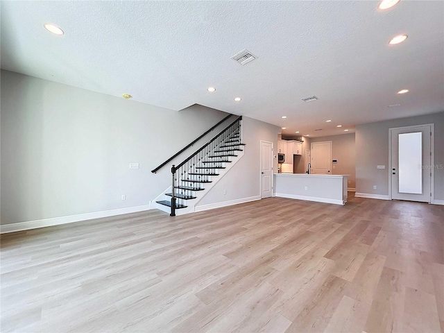 unfurnished living room with visible vents, baseboards, stairs, light wood-style floors, and a textured ceiling