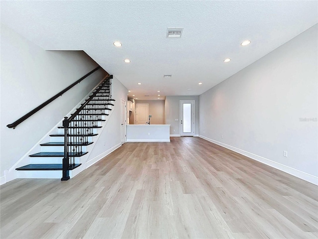 unfurnished living room featuring visible vents, light wood-style flooring, a textured ceiling, stairway, and baseboards