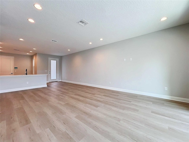 unfurnished living room with baseboards, visible vents, light wood finished floors, and a textured ceiling