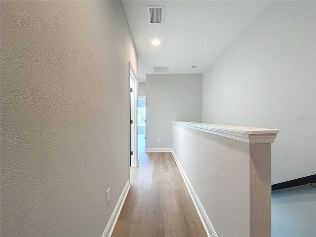 corridor with visible vents, an upstairs landing, wood finished floors, baseboards, and a textured wall