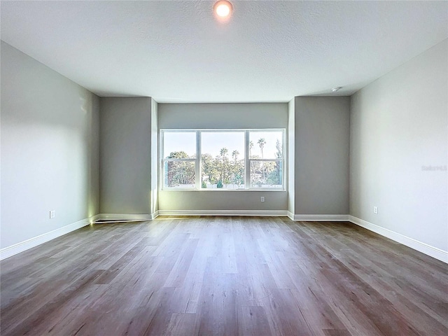 spare room with a textured ceiling, baseboards, and wood finished floors