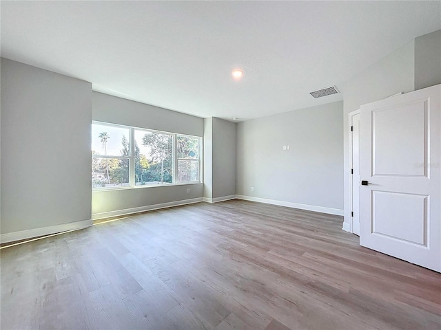 empty room with wood finished floors, visible vents, and baseboards