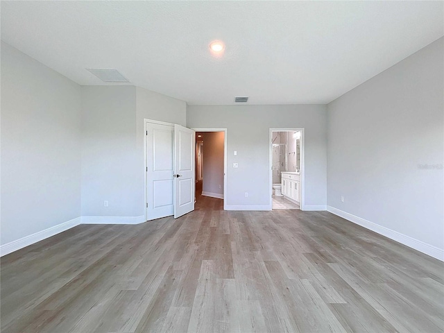 unfurnished bedroom with visible vents, baseboards, ensuite bath, and light wood-style flooring