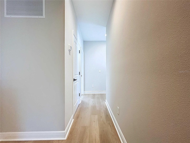 hallway featuring visible vents, baseboards, light wood-style flooring, and a textured wall