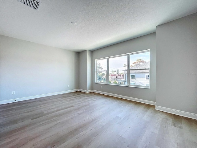 empty room with visible vents, baseboards, dark wood-type flooring, and a textured ceiling