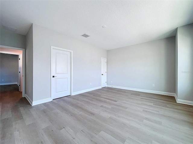 empty room with visible vents, a textured ceiling, baseboards, and wood finished floors