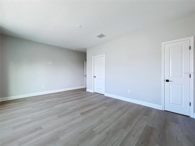 unfurnished room featuring a textured ceiling, wood finished floors, visible vents, and baseboards