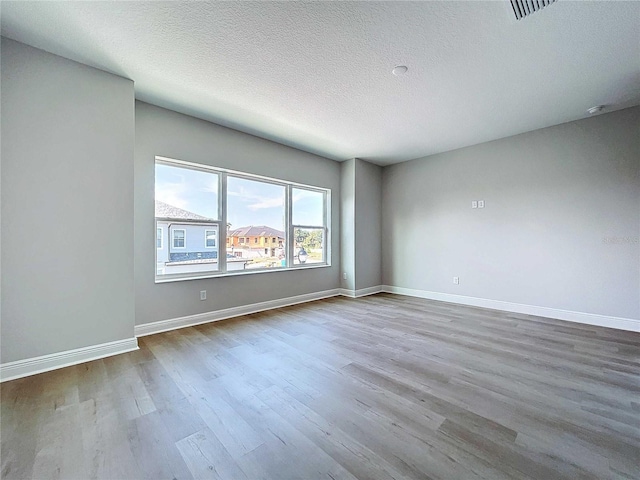 spare room with visible vents, wood finished floors, baseboards, and a textured ceiling