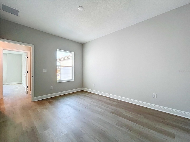 empty room featuring visible vents, baseboards, a textured ceiling, and wood finished floors