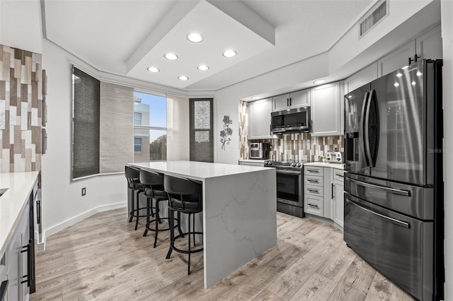 kitchen with a breakfast bar, gray cabinetry, a kitchen island, stainless steel appliances, and backsplash