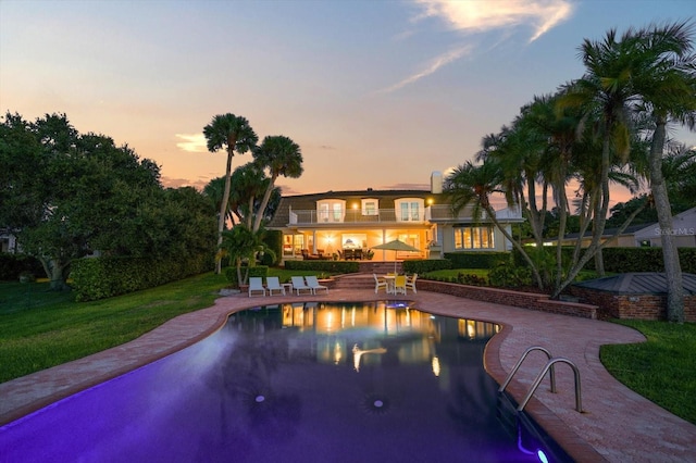 pool at dusk with a patio area and a lawn