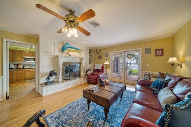 living room with ceiling fan, a premium fireplace, light hardwood / wood-style floors, ornamental molding, and french doors