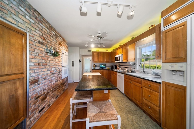 kitchen with white appliances, brick wall, a kitchen island, ceiling fan, and track lighting