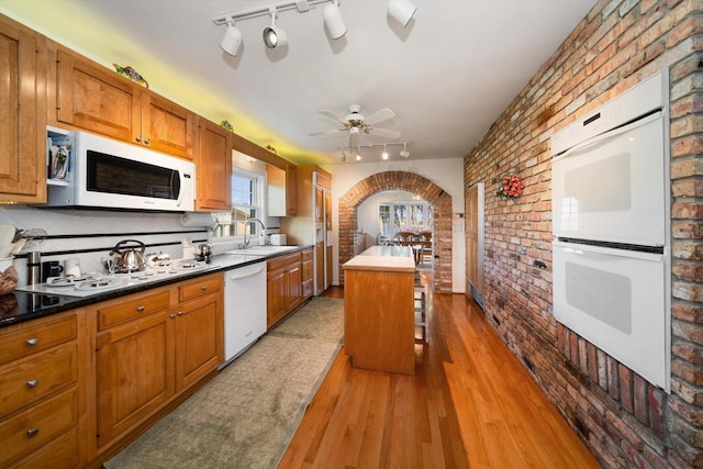 kitchen with rail lighting, light hardwood / wood-style flooring, brick wall, and white appliances