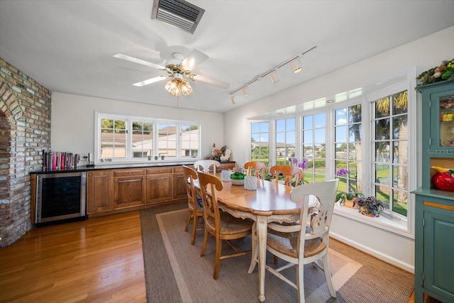 dining room featuring ceiling fan, wine cooler, light wood-type flooring, brick wall, and track lighting