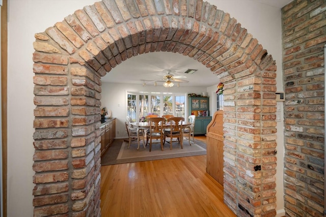 unfurnished dining area featuring brick wall, ceiling fan, and light wood-type flooring