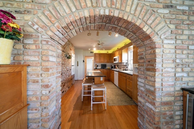 kitchen with a kitchen island, light hardwood / wood-style flooring, ceiling fan, white dishwasher, and brick wall