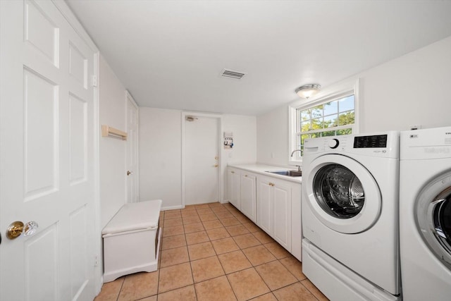 clothes washing area with cabinets, washing machine and dryer, light tile floors, and sink