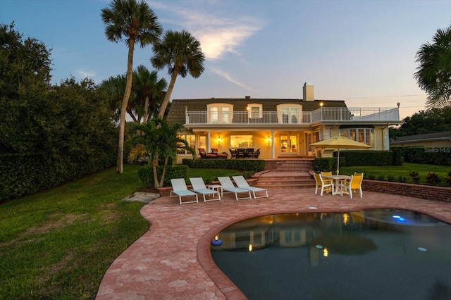 back house at dusk with a patio area, a yard, and a balcony