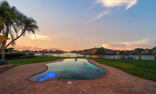 pool at dusk with a water view and a lawn