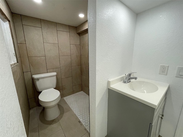 bathroom with toilet, vanity, tile walls, tile floors, and a tile shower