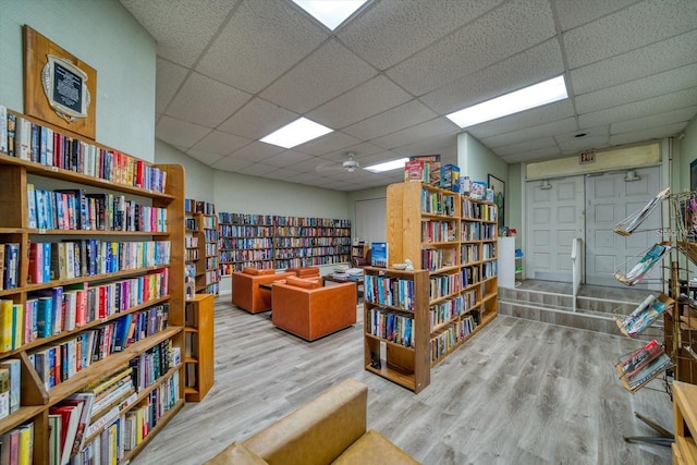 interior space featuring a drop ceiling, wall of books, and wood finished floors