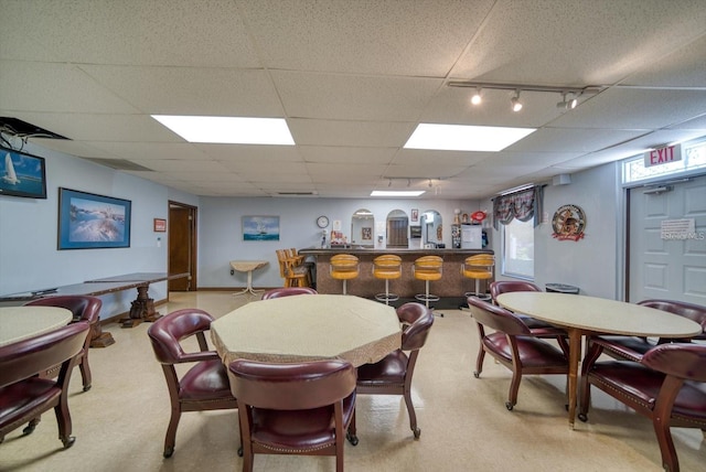 carpeted dining space featuring bar, track lighting, and a drop ceiling