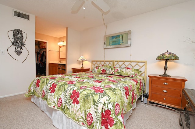 bedroom with ceiling fan, a spacious closet, light colored carpet, ensuite bathroom, and a closet