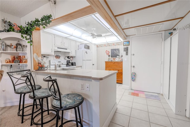 kitchen featuring a peninsula, under cabinet range hood, a sink, light tile patterned floors, and freestanding refrigerator