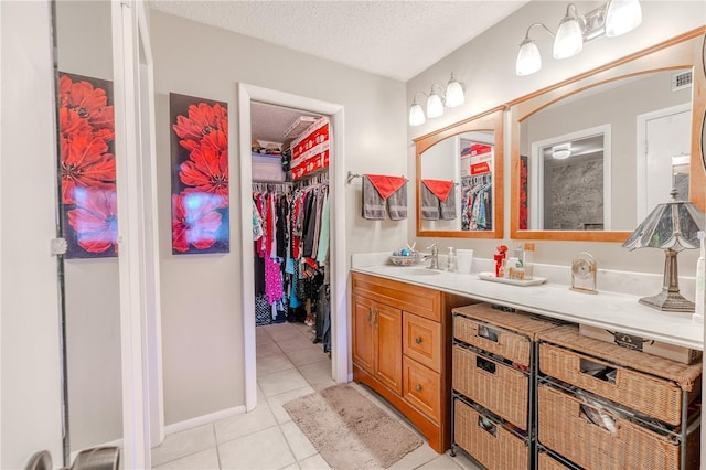 bathroom with tile patterned floors, vanity, a walk in closet, a textured ceiling, and visible vents
