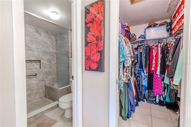 bathroom with tile patterned floors, toilet, tiled shower, a spacious closet, and a textured ceiling