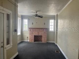 unfurnished living room featuring crown molding, a brick fireplace, ceiling fan, and dark colored carpet