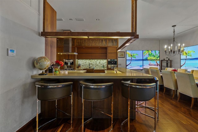 bar with a notable chandelier, decorative light fixtures, dark hardwood / wood-style floors, and wall chimney exhaust hood