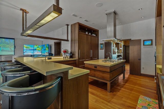 kitchen with stainless steel gas cooktop, island range hood, an island with sink, and light wood-type flooring