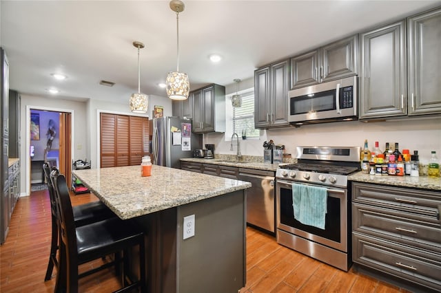 kitchen with a kitchen island, stainless steel appliances, decorative light fixtures, light stone countertops, and a kitchen bar