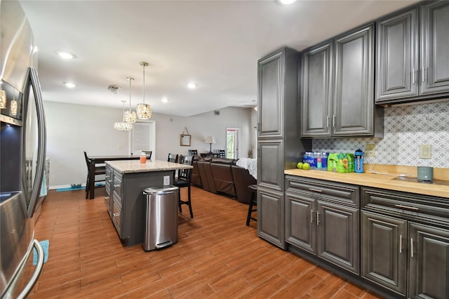 kitchen with decorative light fixtures, a notable chandelier, a kitchen bar, tasteful backsplash, and stainless steel fridge