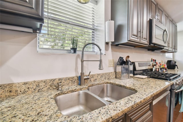 kitchen featuring light stone counters, stainless steel appliances, and sink