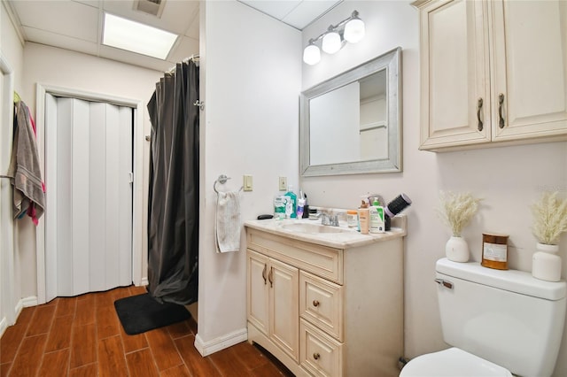 bathroom featuring hardwood / wood-style floors, a drop ceiling, vanity with extensive cabinet space, and toilet