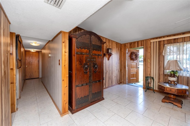 entrance foyer with wood walls, a textured ceiling, and light tile floors