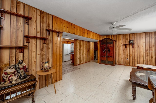 sitting room with wood walls, a textured ceiling, ceiling fan, and light tile floors