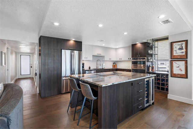 kitchen with dark wood-type flooring, stainless steel appliances, a center island, white cabinetry, and a textured ceiling