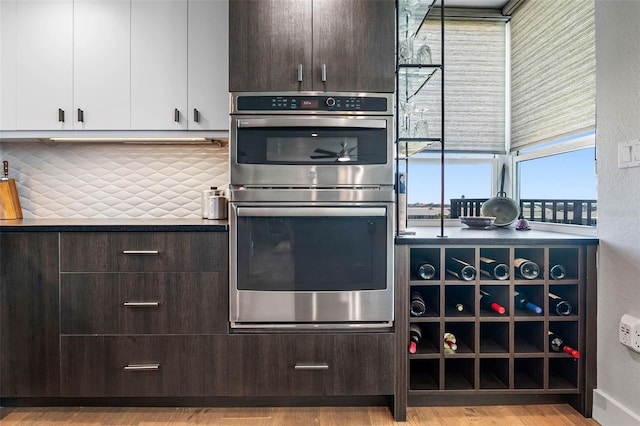 kitchen with backsplash, white cabinetry, light hardwood / wood-style flooring, dark brown cabinetry, and double oven