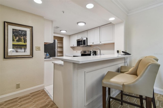 kitchen featuring a breakfast bar, kitchen peninsula, ornamental molding, appliances with stainless steel finishes, and white cabinetry