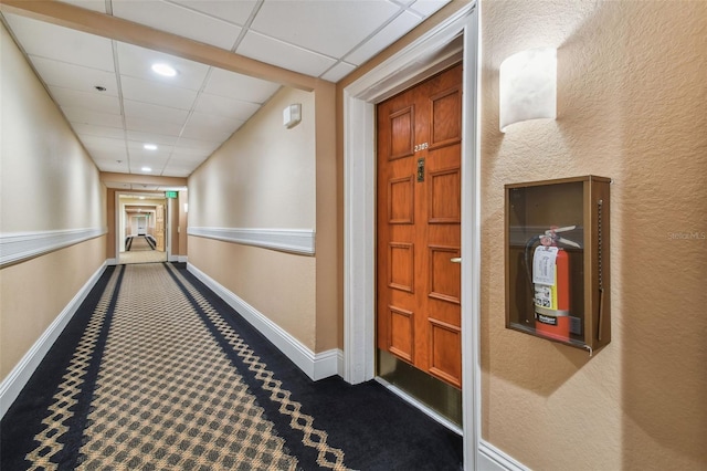 hall with dark colored carpet and a paneled ceiling