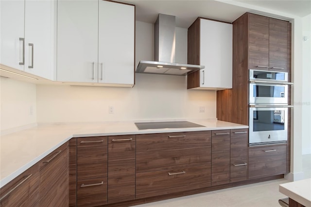 kitchen with light tile floors, stainless steel double oven, white cabinets, black electric cooktop, and wall chimney range hood