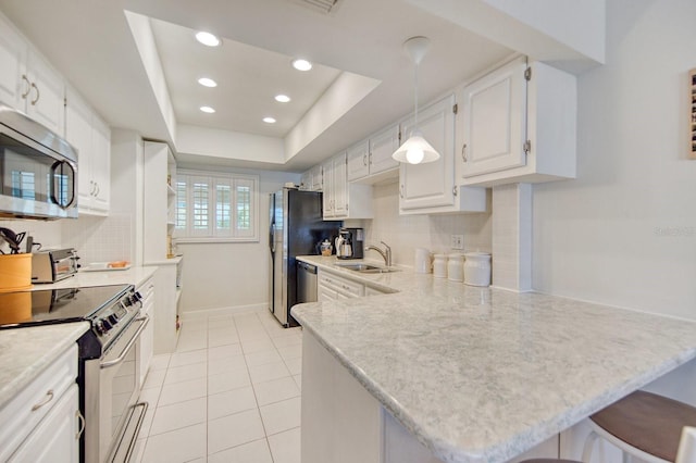 kitchen featuring a breakfast bar, white cabinetry, appliances with stainless steel finishes, a tray ceiling, and kitchen peninsula