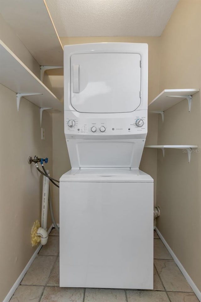 washroom with stacked washing maching and dryer, a textured ceiling, and light tile patterned floors