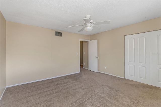 unfurnished bedroom featuring ceiling fan, light colored carpet, a closet, and a textured ceiling